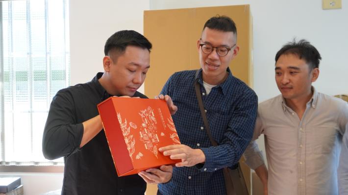 攜手大樹麻油行設計品牌新樣式的 「高雄的囝仔就是我」團隊設計師張鈞豪(中)，仔細向高市青年局長張以理(左)介紹年節禮盒包裝的設計概念。