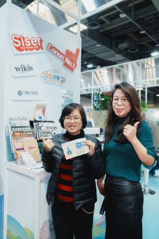 高雄市青年局副局長汪小芬(左)與來自高雄的「威齊織品科技」交流，並於現場體驗以環保熱轉印技術輸出的「米台北+高雄85大樓地標」特色筆袋。