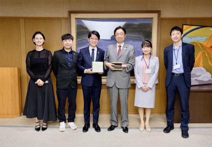 圖說一：高雄市青年局長林楷軒（左三）率團拜會日本熊本縣知事木村敬（右三），致贈高雄青創基地業者「大雄的木作世界」客製化手工木屐筆，熊本則以當地特製伴手禮回贈致意。